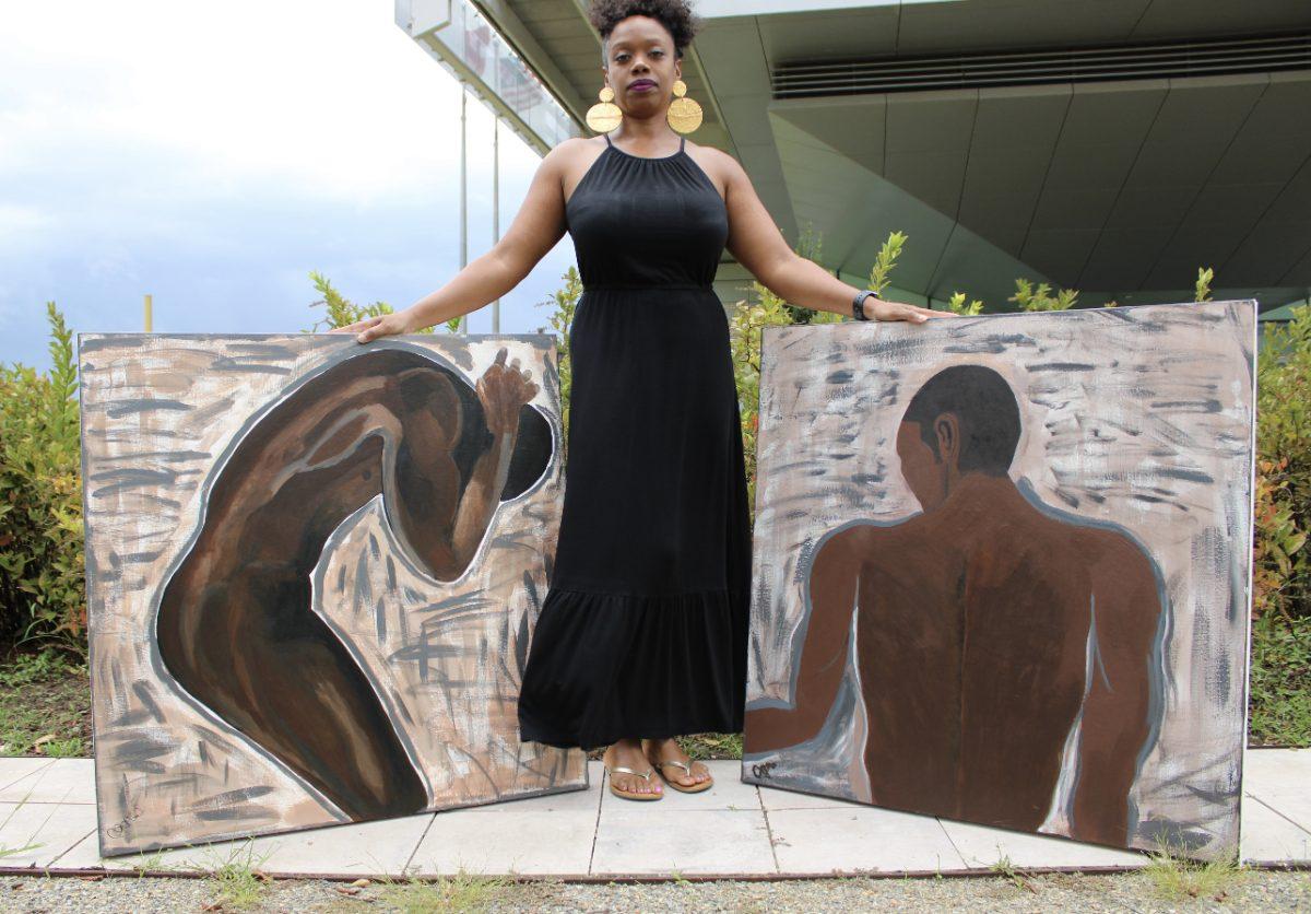 Cozetta Jones, owner of Art by Cozi, standing by two original acrylic paintings titled, “On Our Backs” and “It’s My Strength”.