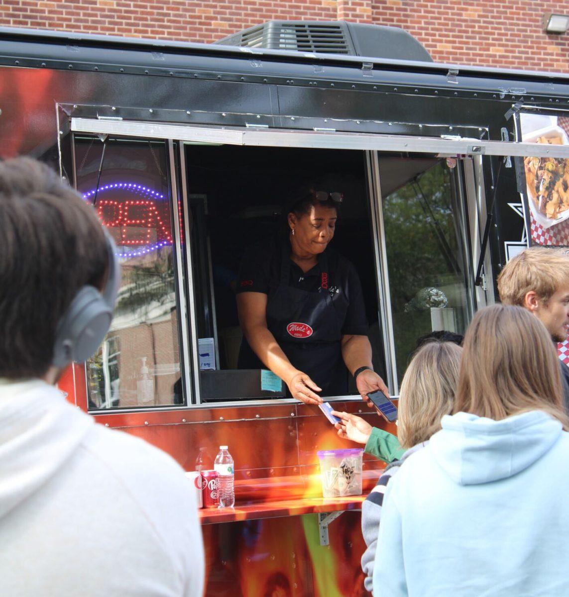 A Wade’s BBQ worker hand’s a student her card. Ten food trucks gathered on campus for a celebratory festival. Students voiced desire for more food trucks on campus.