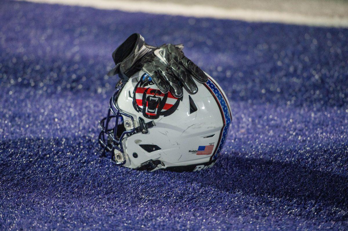 A UCA helmet rests on the ground with a players gloves set on top.