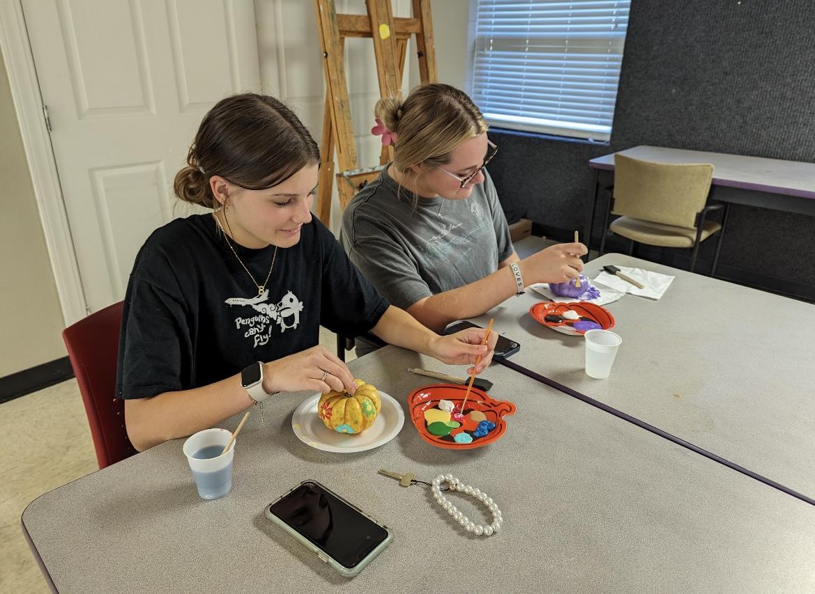 Two students paint mini pumpkins with acrylic paint at the Arkansas Hall event. Students had creative freedom over their pumpkins, painting anything from cartoon characters to floral patterns.