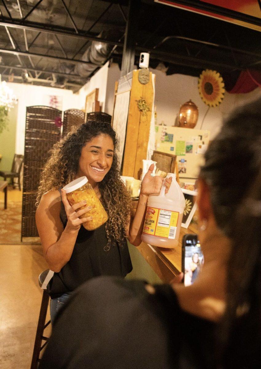 Sara Alawadhi smiles with her jar of fire cider and a jug of apple cider vinegar while Jelaya Fairfield takes her picture. 