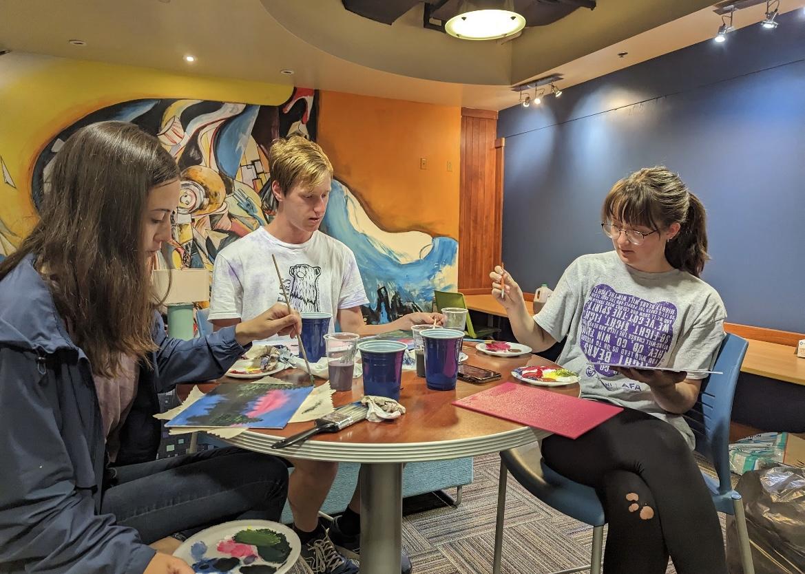 (Left to right) Freshmen Kira Rich, Connor Dow and Taryn Wells paint along to a Bob Ross tutorial. The Honors College served chicken and waffles at the event.