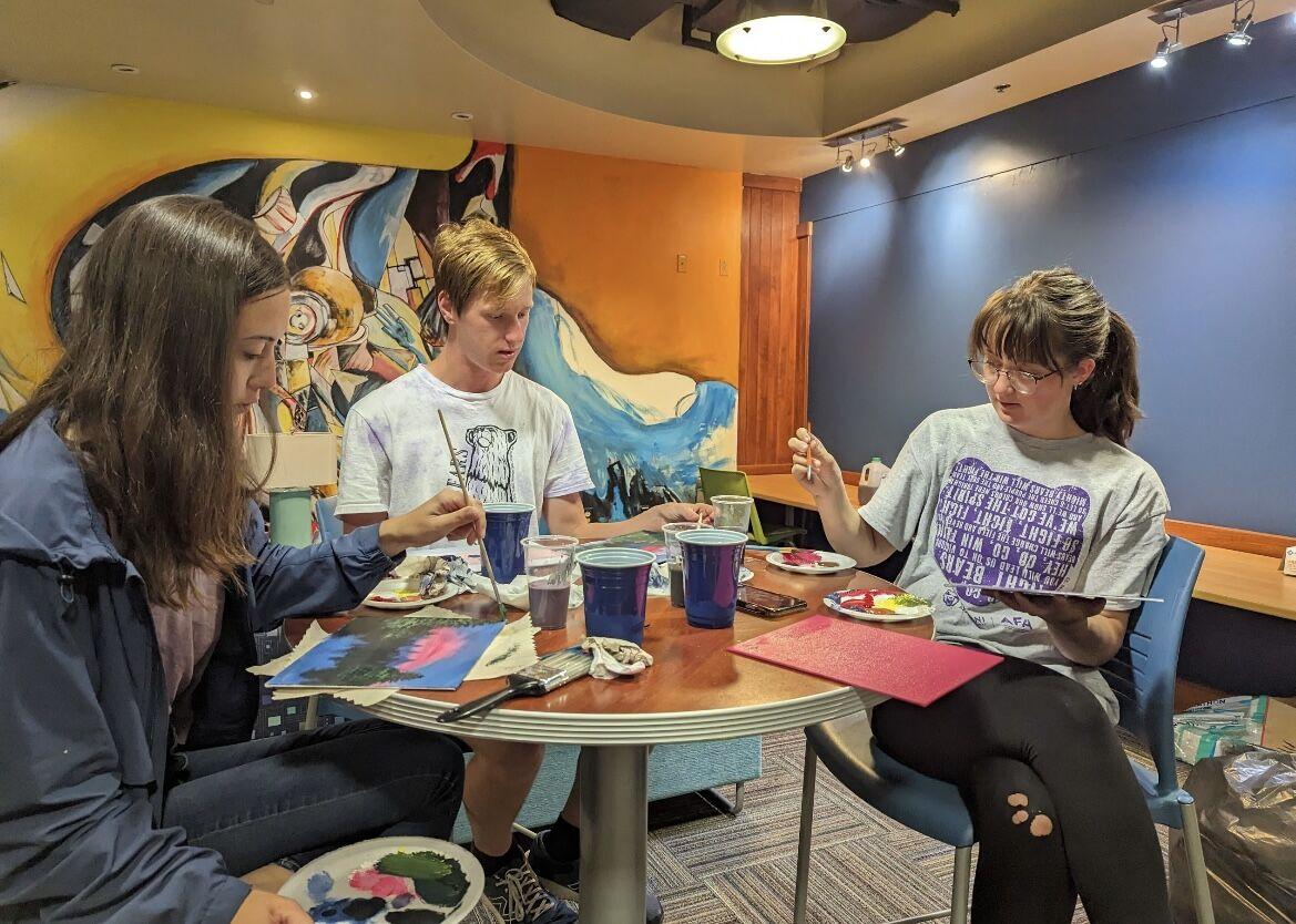 (Left to right) Freshmen Kira Rich, Connor Dow and Taryn Wells paint along to a Bob Ross tutorial. The Honors College served chicken and waffles at the event.