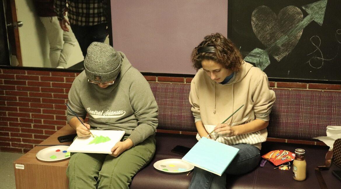 Two students paint on canvases Nov. 28 at the Bernard Hall Coffee and Canvas event. Attendees used acrylic paint to make various nature scenes.