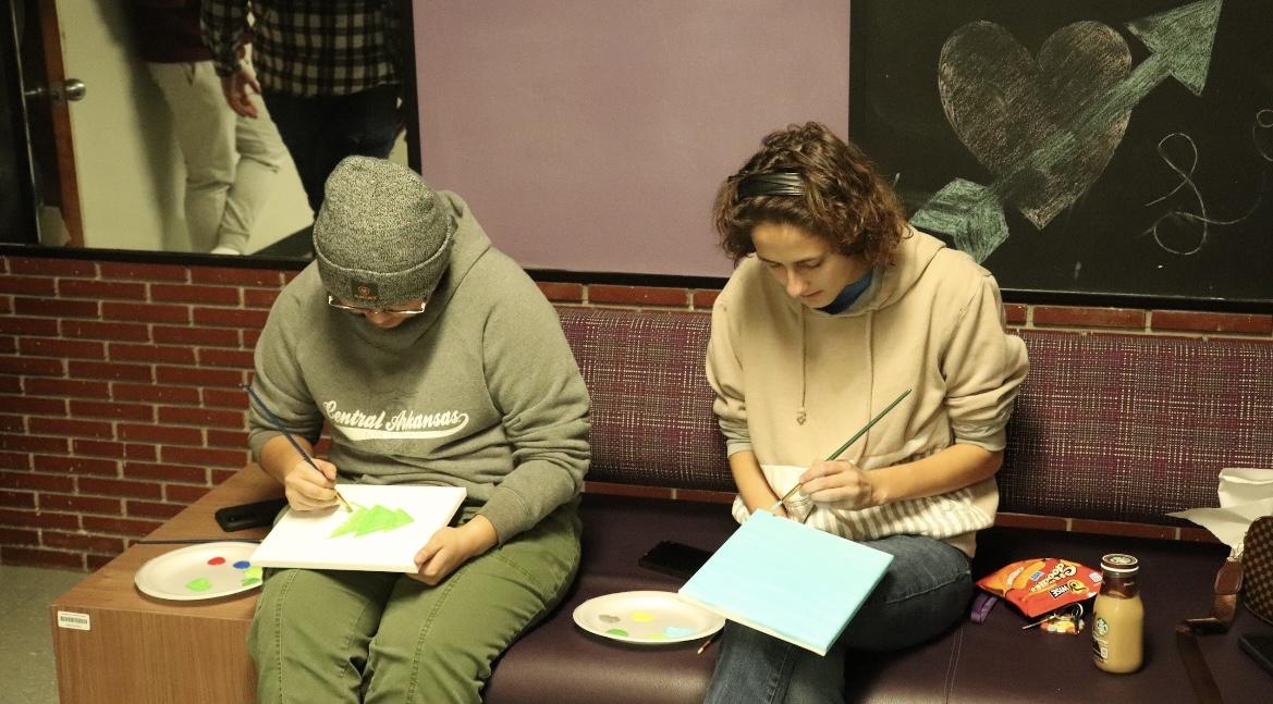 Two students paint on canvases Nov. 28 at the Bernard Hall Coffee and Canvas event. Attendees used acrylic paint to make various nature scenes.