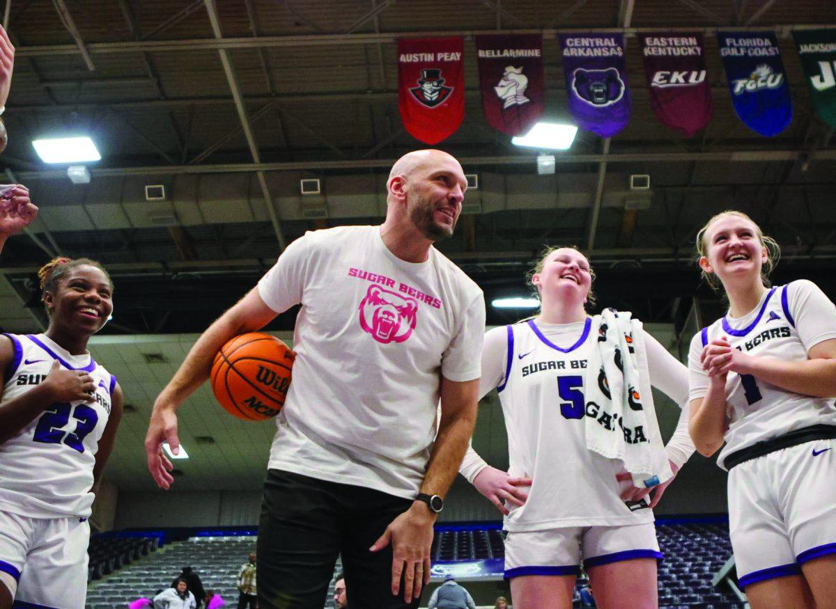 (Left) Freshman guard Kaidyn Beckwith, (center) coach Tony Kemper, (center) junior forward Bree Stephens and (right) junior guard Kinley Fisher smile together after their win. The Sugar Bears have won all 10 of their home games so far this season.