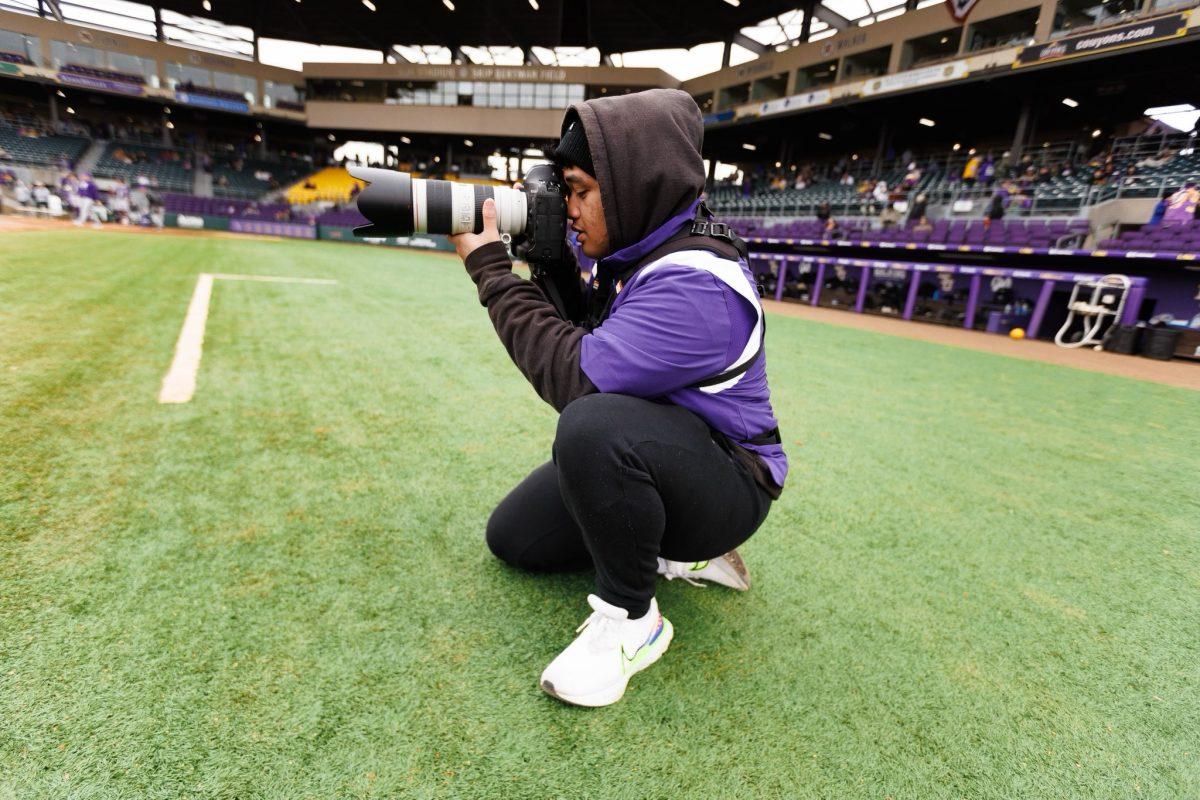 Junior Jhude Dizon kneels on one knee to take a photo. Dizon is a photographer for several Arkansas sports teams, as well as UCA Athletics. (photo courtesy of @jdizon02 on X) 