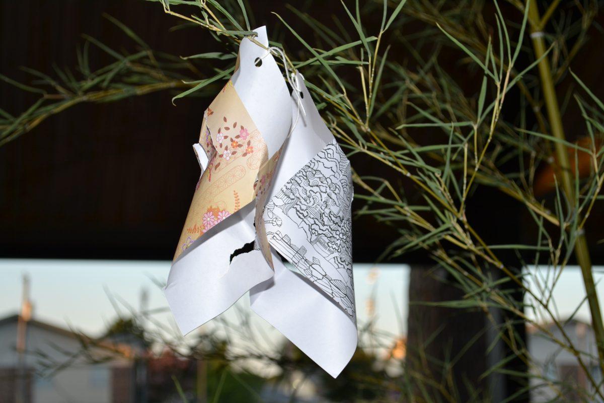 A patterned piece of paper with wishes written on it, tanzaku, hangs off of a bamboo pole. 