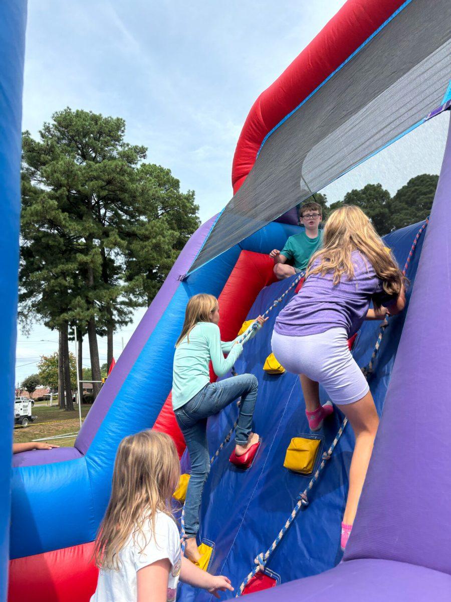 Children climb on bouncy house during Family Weekend at the football practice field. Three girls climb up the bouncy house while a young boy sits at the top. 