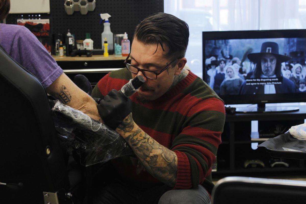 Tattoo artist, Guillermo Martinez, can be seeing inking art on an event attendee. On Halloween day creatively spooky designs thrived.  (photo by Vivian Phillips )