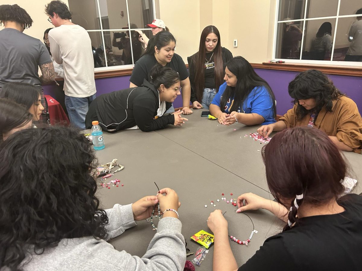 A group of students admires another student's bracelet. In addition to charm-making, Sigma Iota Alpha played upbeat music, with a playlist featuring artists such as Bad Bunny.